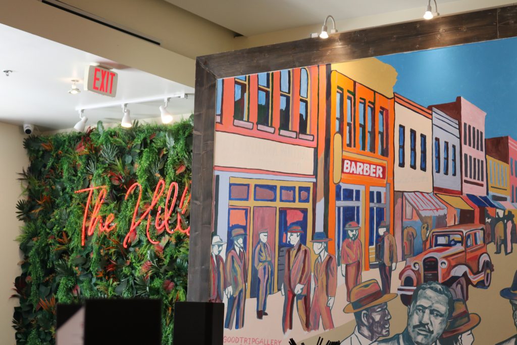 Interior of the Flavor Hills Restaurant. Mural to the right of a floral background with neon sign reading "The Hills."